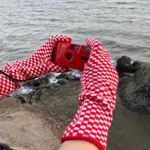 Close-up detail of red and white checkered knit gloves worn outdoors near the sea scenic view.