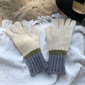 Close-up of minimalist color-block knit gloves with ribbed cuffs on sandy blanket background.