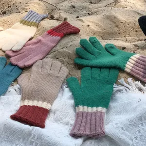 Detail shot of colorful knit gloves displayed on sand and fabric, showing texture and color variety.
