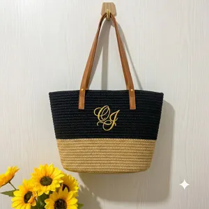 Detail view of a stylish woven tote bag with embroidered monogram and contrast straps.