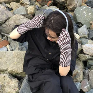 Outdoor detail shot of brown and white checkered knit gloves worn by model on rocks background.