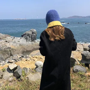 Outdoor detail view of a blue and yellow color block knit balaclava hat worn near the sea.