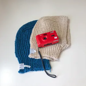 Detailed view of knitted balaclava beanies in blue and beige tones, featuring texture and label.