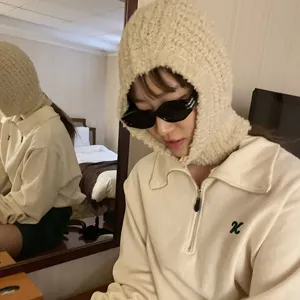 Closeup detail of cozy beige knitted balaclava hood worn in indoor scene, soft warm texture.