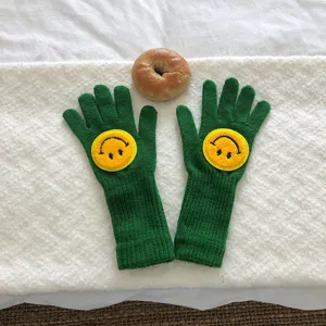 Gros plan de gants en tricot vert avec une broderie de smiley jaune mignon sur blanc.