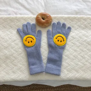 Vue en gros plan de gants en tricot bleu clair avec de jolis écussons smiley jaunes.