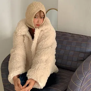 Detail shot of a cozy beige knitted balaclava hood worn with a fluffy winter fleece jacket indoors.