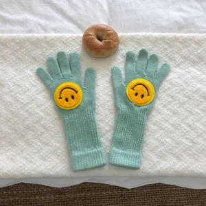 Vue détaillée de gants d'hiver en tricot vert menthe avec émojis souriants jaunes.
