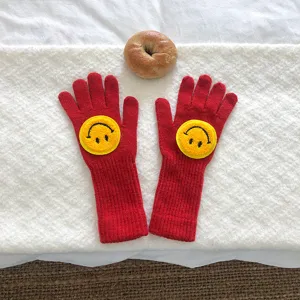 Gros plan de gants en tricot rouge avec broderie smiley jaune, joli détail d'hiver.