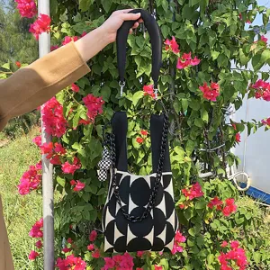Gros plan sur le sac bandoulière en tricot noir et blanc avec chaîne et joli pendentif.