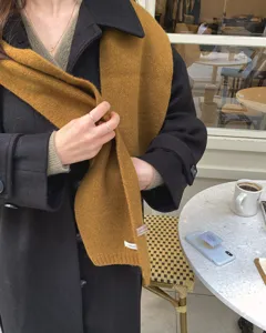 Detailaufnahme eines einfarbigen Wollschals getragen mit schwarzem Mantel in einem Café.