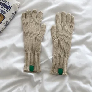 Primer plano de guantes de punto lisos, puños acanalados con detalle de etiqueta verde.
