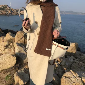 Primer plano detallado de una elegante bufanda de punto marrón usada junto al mar.