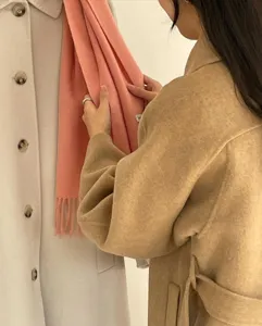 Toma de detalle de una bufanda de lana lisa con fleocos en rosa suave, textura y diseño.