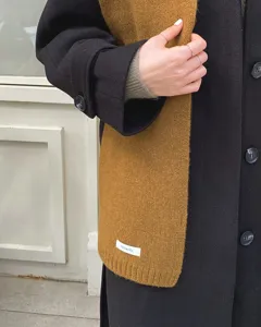 Nahaufnahme eines dicken, senfgelben Wollstrickschals, elegant getragen zu einem schwarzen Mantel.