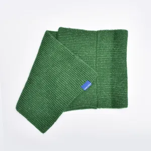 Close-up detail of a solid green knitted wool cross scarf with a small blue brand label.