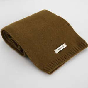 Detailaufnahme des braunen Wollschals mit weicher Textur und feinem 100% Wolle Etikett.