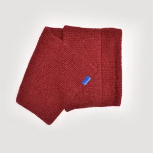 Detail view of a cozy red knit wool cross neck warmer scarf with a small blue label.