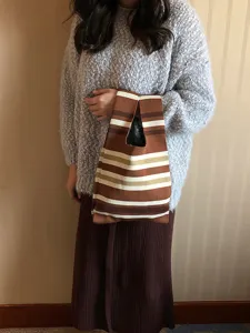 Dettaglio di una borsa shopper in maglia a righe marroni tenuta dal modello, stile quotidiano.