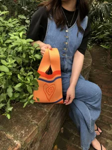Orange knit tote bag with blue stripes and spiral heart pattern shown in outdoor lifestyle scene.
