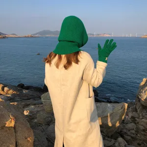 Gedetailleerd overzicht van de groene gebreide bivakmuts en bijpassende handschoenen aan zee.