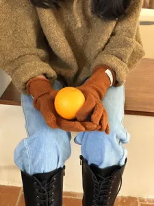 Detailaufnahme von warmen braunen Strickhandschuhen mit Etikett beim Halten einer Orange.