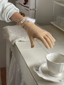Nahaufnahme warmer Damen-Knitted-Handschuhe in Beige mit weißem Plüsch-Pompon und Label.