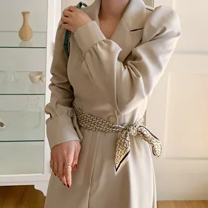 Close-up detail of stylish beige blazer dress with vintage chain print silk scarf belt.