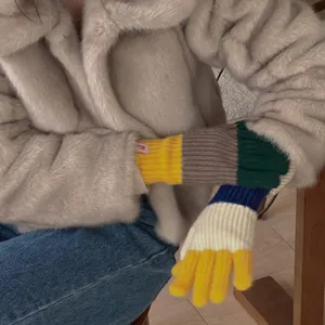 Close-up detail of women's colorful knitted winter five-finger gloves worn with cozy jacket.