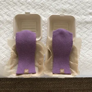 Dettaglio ravvicinato di guanti invernali lavorati a maglia viola esposti nelle scatole.