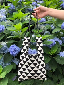 Vista di dettaglio della borsa tote in maglia geometrica bianco e nero tra ortensie blu.