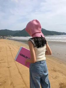 Vue détaillée de la cagoule en laine rose sur la plage de sable, idéale pour l'automne et l'hiver.