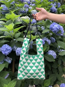 Vista dettagliata di borsa tote in maglia geometrica verde e bianca con manici in giardino.