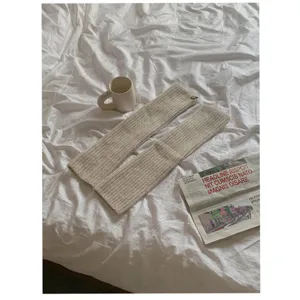 Gedetailleerd shot van beige gebreide beenwarmers op wit laken met mok en krant.