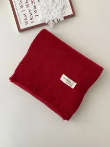 Rotes Strickschal Detail mit weicher Wolle Textur und handgemachtem Modelabel auf Tisch.