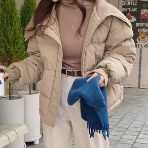 Piumino invernale caldo e ispessito abbinato a maglione in maglia e sciarpa da donna chic.