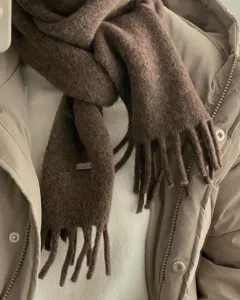 Primo piano sulla morbida texture della sciarpa invernale in lana e dettagli delle frange.