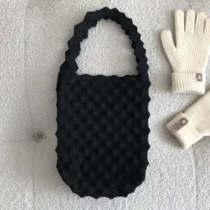 Close-up van zwarte gebreide handtas met gewolfde handgreep op zachte witte achtergrond.