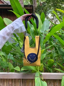 Detailansicht der gelben gestrickten Handtasche mit blauem Smiley, Kette und Anhänger.