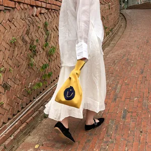 Detailaufnahme einer gelben Stricktasche mit einem blauen Smiley-Gesicht für den Alltag.