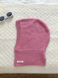 Gros plan détaillé d'un bonnet cagoule en laine tricotée rose doux avec étiquette 100% laine.