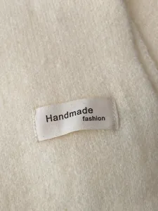 Nahaufnahme des cremefarbenen Strickschals mit weicher Wolltextur und handgefertigtem Etikett.