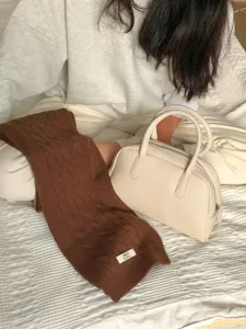 Nahaufnahme des weichen braunen Strickschals mit feiner Textur auf gemütlichem Bett.