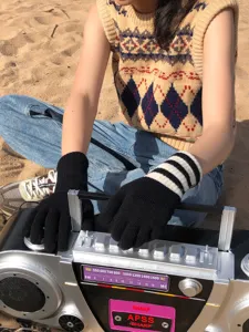 Detailansicht der kuscheligen schwarzen und gestreiften Strick-Touchscreen-Handschuhe am Strand.