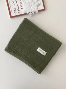 Nahaufnahme eines kuscheligen grünen Winterschals mit Handmade-Label, sauber gefaltet.