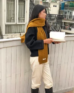 Detailaufnahme eines kuscheligen Winterschal in Senfgelb, weiche Zopfstrick-Textur.