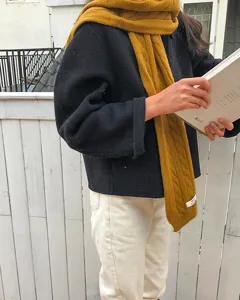 Detailansicht eines kuscheligen gelben Strickschals mit klassischem Zopfmuster, Outdoor-Look.