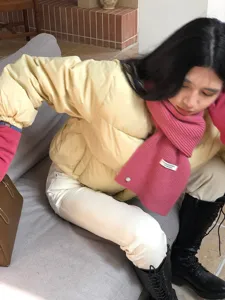 Detaillierte Nahaufnahme eines kuscheligen rosa Strickschals, getragen in einem warmen Raum.