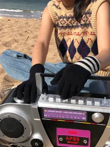 Nahaufnahme von schwarzen Strickhandschuhen mit gestreifter Manschette am sonnigen Strand.