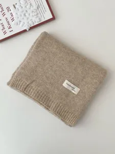 Detailansicht eines kuscheligen khakifarbenen Strickschals, ordentlich gefaltet mit Etikett.